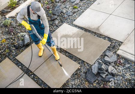 Proprietario di casa caucasica nel suo 40s lavatrice fuori la sporcizia dai suoi sentieri di cemento del giardino usando la rondella di pressione. Giardino moderno piccola architettura manutenzione. Foto Stock