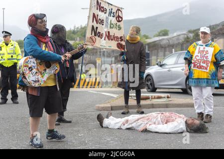 Coulport, Argyll, Scozia 13 giugno 2022 cinque ex donne di Greenham e tre membri di Peace Pirates, un'offshoot di parti di guerra Trident, palcoscenico un blocco presso il negozio di teste di guerra nucleare di Coulport. Il «Greenham versava sangue falso su se stesso e ha messo in scena un morso davanti alle porte, bloccando un lato dell'ingresso nella base, mentre i membri dei «Pirati della Pace» (insegnante in pensione Brian Quail, 84, con un trapianto di cuore e disabilitato da un recente colpo, Willemien Hoogendorf dall'Olanda e Gillean Lawrence, nonna e sostenitrice di XR Peace) bloccati a bloccare la rotatoria più avanti Foto Stock