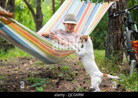 Donna caucasica si trova in un'amaca con Jack Russell Terrier cane in una pineta Foto Stock