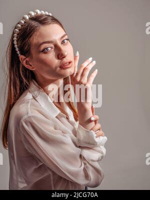Giovane donna elegante in casuali bianchi che guardano via e sorridenti. Verticale Foto Stock