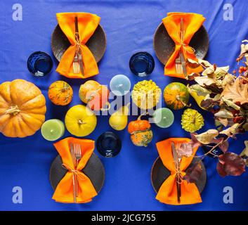 Tavola di ringraziamento, bouquet con rami secchi, zucche e candele, piatti con posate e tovaglioli e bicchieri su una tovaglia blu-viola Foto Stock