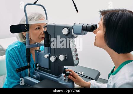 Optometristo femminile che fa il test della vista alla donna anziana alla clinica moderna di oftalmologia. Esame visivo e diagnostica visiva Foto Stock