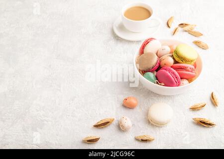 Macaroon multicolore e uova di cioccolato in ciotola di ceramica, tazza di caffè su sfondo grigio di cemento. Vista laterale, spazio copia, natura morta. Colazione Foto Stock