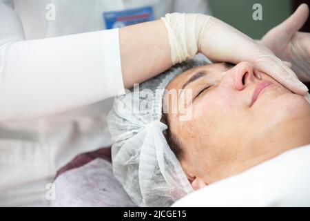 Primo piano di un medico cosmetologo che fa una procedura anti-invecchiamento, maschera e peeling ad un cliente anziano in una clinica di bellezza. Specialista della cura della pelle. COSM Foto Stock