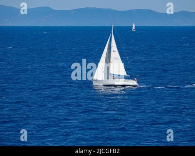 Barche a vela nell'arcipelago toscano, navigando tra la costa d'Elba e l'Italia continentale con montagne sullo sfondo. Foto Stock