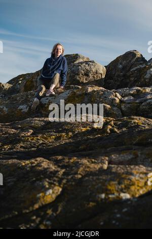 Una donna siede sulle rocce costiere dell'oceano. Foto Stock