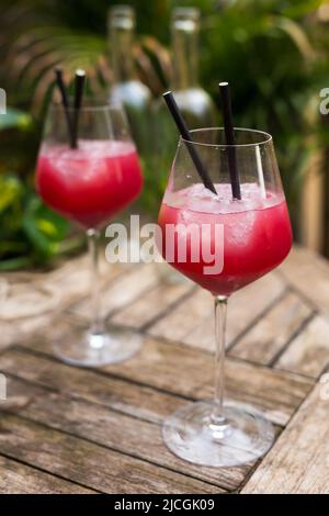 cocktail rosso con ghiaccio in vetro con gambo su superficie di legno Foto Stock