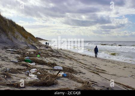 Spazzatura e bottiglie di plastica sulla spiaggia. La spazzatura buttata fuori da una tempesta. Persone a piedi. Mar Baltico in inverno Foto Stock