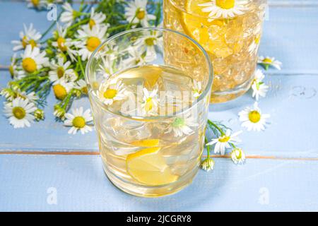 Bevanda fredda biologica a base di erbe. Infuso di acqua di fiore. Tè o limonata alla margherita ghiacciato con fette di limone e cubetti di ghiaccio, in due bicchieri diversi, blu w Foto Stock