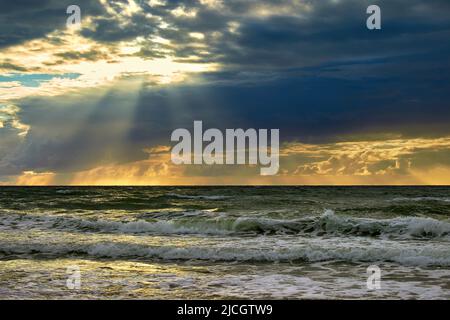 Il mare e i raggi del sole fanno il loro senso attraverso le nuvole. Tramonto sul Mar Baltico Foto Stock