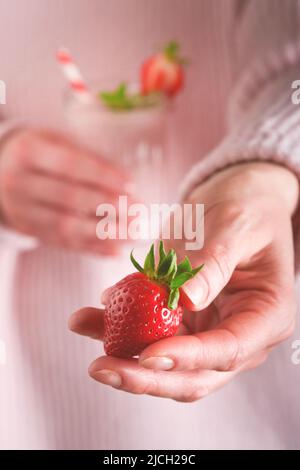 Fragola. Donna che tiene fragola fresca di fragola sullo sfondo di vetro vegan frullato da fragola, banana, semi di chia e menta. Mangiare pulito Foto Stock