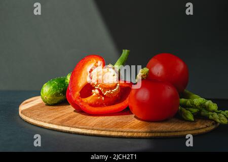 rami di asparagi verdi freschi, peperoni, pomodori e cetrioli su un asse di legno, sfondo grigio scuro, vista dall'alto. Concetto di tendenza di base con spazio di copia Foto Stock