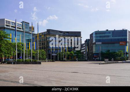 Parco commerciale su una piazza con un lago. Molti flagpoli con bandiere ucraine di fronte agli edifici commerciali. Colonia, Germania, 22.5.22 Foto Stock