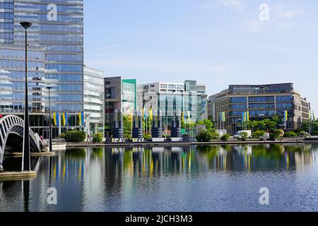 Parco commerciale su una piazza con un lago. Molti flagpoli con bandiere ucraine di fronte agli edifici commerciali. Colonia, Germania, 22.5.22 Foto Stock