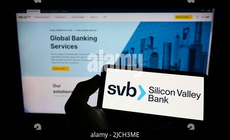 Persona che tiene il cellulare con il logo della società finanziaria americana Silicon Valley Bank (SVB) sullo schermo di fronte alla pagina web. Mettere a fuoco sul display del telefono. Foto Stock