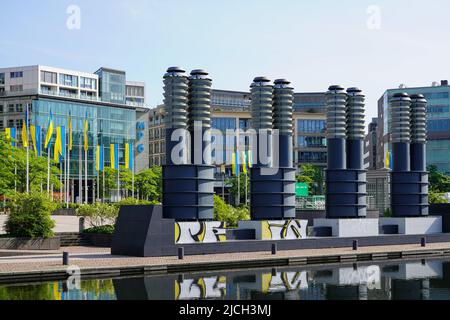 Parco commerciale su una piazza con un lago. Molti flagpoli con bandiere ucraine di fronte agli edifici commerciali. Colonia, Germania, 22.5.22 Foto Stock