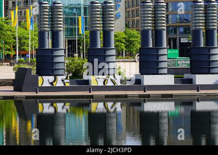 Parco commerciale su una piazza con un lago. Molti flagpoli con bandiere ucraine di fronte agli edifici commerciali. Colonia, Germania, 22.5.22 Foto Stock