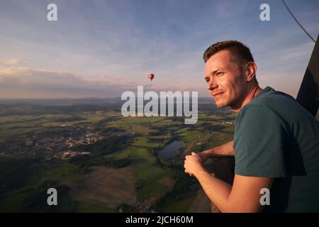 Uomo che gode dalla vista da mongolfiera durante il volo sopra il paesaggio bello al tramonto. Temi avventura, libertà e viaggi. Foto Stock