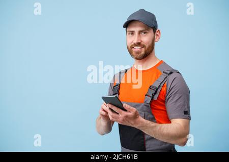 Sorridente lavoratore maschio in uniforme tenere il cellulare e guardare la fotocamera Foto Stock