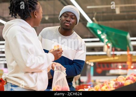 Giovane uomo con carrello che guarda la mela fresca tenuta dalla sua ragazza scelta frutta nel reparto di alimentari del supermercato Foto Stock