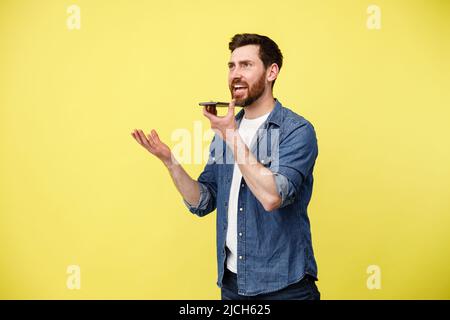 Bell'uomo che registra il messaggio vocale sul telefono su sfondo giallo Foto Stock