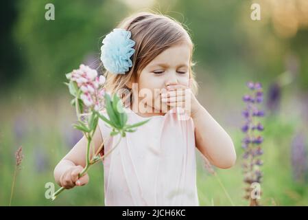 ritratto di carino ragazza bambino felice di due anni con fiori lupini in fiore in campo di fiori viola. Bambino in natura concetto. Vacanze estive. Stagione di allergia primaverile. Infanzia Foto Stock