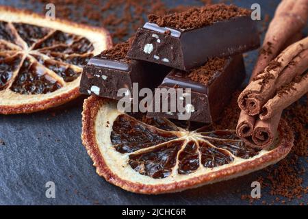 Cioccolato fondente con mandorle tritate, cacao in polvere, fette di arancia secca e bastoncini di cannella. Primo piano. Giorno di cioccolato fondente Foto Stock