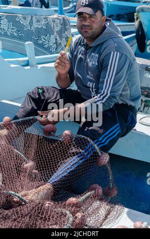 Hurghada, Egitto - 21 febbraio 2022: Pescatore cucire reti da pesca nel porto egiziano Foto Stock