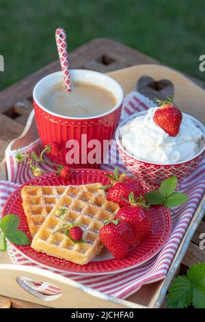 waffle e fragole fresche sul piatto, tazza di caffè e panna montata Foto Stock