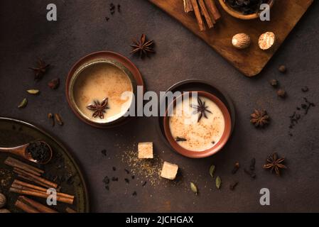 Masala Chai Tea in tazza di ceramica con ingredienti. Tradizionale tè nero speziato indiano con latte su sfondo rustico scuro Foto Stock