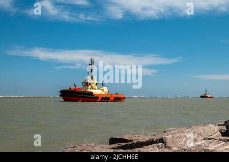 Due rimorchiatori che navigano dal mare in un canale di navigazione dopo aver guidato una petroliera, in una giornata di sole con cielo blu e alcune nuvole. Foto Stock