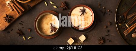 Masala Chai Tea in tazza di ceramica con ingredienti. Tradizionale indiano speziato tè nero con latte su sfondo rustico scuro, banner Foto Stock