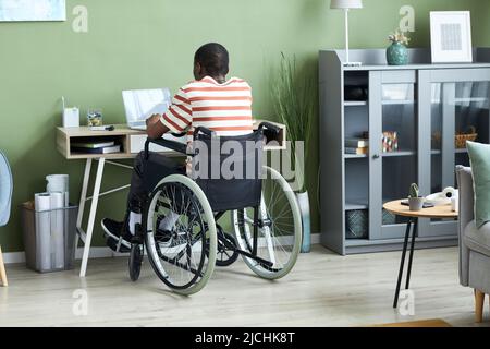 Indietro consente di visualizzare il ritratto dell'uomo afro-americano in sedia a rotelle utilizzando un computer portatile e scrivendo un codice mentre si lavora da casa, spazio copia Foto Stock