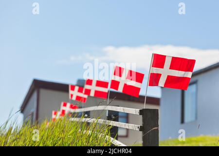 Bandiere bianche su rosse danesi in fila su una recinzione di legno in un villaggio scandinavo durante le festività nazionali Foto Stock