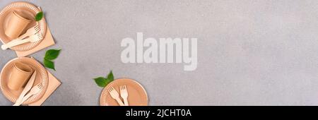 Banner con set di carta e stoviglie in legno - tazze in carta, piatti e posate in bambù su sfondo grigio in calcestruzzo con spazio per la copia del testo. Sostenga Foto Stock
