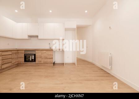 Cucina ristrutturata di recente con armadi in legno, ripiani in legno con elettrodomestici neri e armadi superiori bianco lucido, pareti dipinte di bianco e opaco Foto Stock