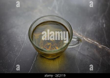 Tè verde alle erbe in una tazza trasparente su sfondo scuro Foto Stock