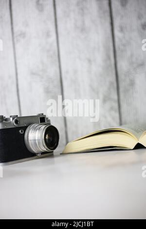 Fotocamera vintage accanto a un libro aperto su sfondo chiaro Foto Stock