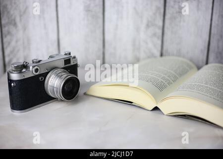 Fotocamera vintage accanto a un libro aperto su sfondo chiaro Foto Stock