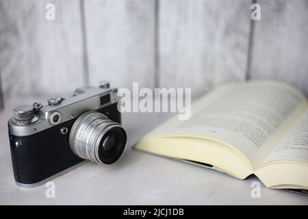 Fotocamera vintage accanto a un libro aperto su sfondo chiaro Foto Stock