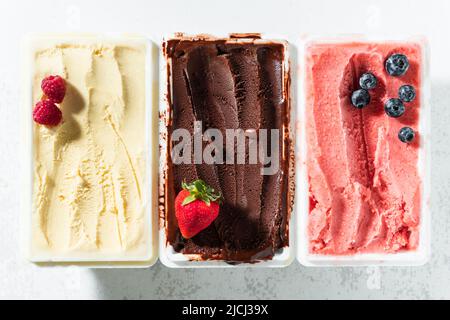 Vero gelato artigianale italiano in confezione: Cioccolato, fragole, vaniglia con frutti di bosco e un cucchiaio Foto Stock