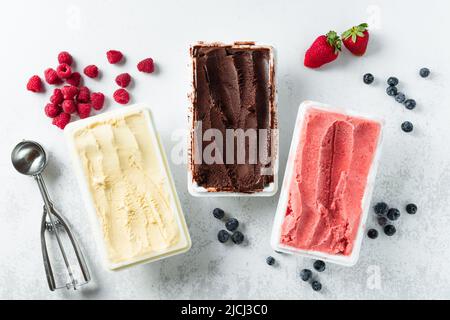 Vero gelato artigianale italiano in confezione: Cioccolato, fragole, vaniglia con frutti di bosco e un cucchiaio Foto Stock