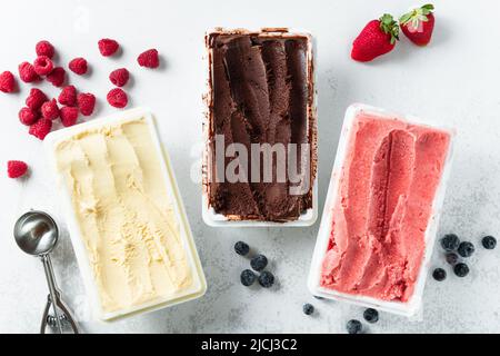 Vero gelato artigianale italiano in confezione: Cioccolato, fragole, vaniglia con frutti di bosco e un cucchiaio Foto Stock