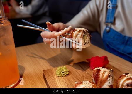 Giovane donna corto 20s indossare abiti casual tenere in mano makizushi sushi rotolo servito su piatto tradizionale cibo giapponese Foto Stock