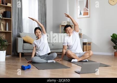 Uomo e donna asiatici sportivi che si esercitano a casa, utilizzando il notebook Foto Stock