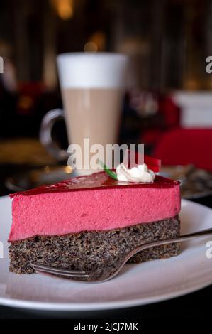 Pezzo di famosa torta di semi di papavero con mousse di lamponi di origine austriaca servito con panna montata e una tazza di caffè latte in vecchio classico caffè-ristorante Foto Stock