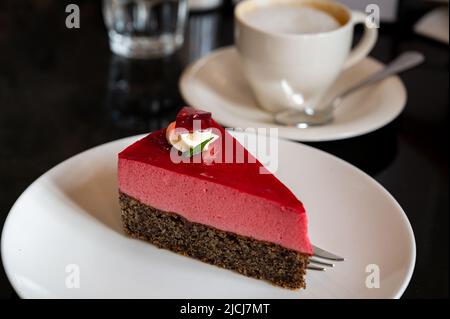 Pezzo di famosa torta di semi di papavero con mousse di lamponi di origine austriaca servito con panna montata e tazza di caffè in vecchio classico caffè-ristorante in Foto Stock