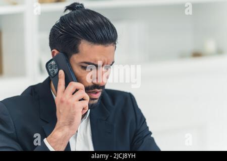 Annoiato pettinato bel uomo cubano che indossa un abito nero e una camicia bianca che parla al telefono, parlando di affari. Foto di alta qualità Foto Stock