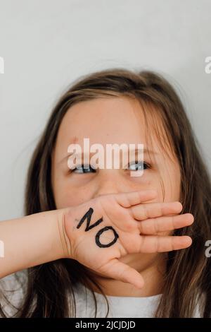 ritratto di piccola ragazza livida spaventato alzando la mano per coprire la bocca, mostrando l'iscrizione no sul palmo aperto. Foto Stock