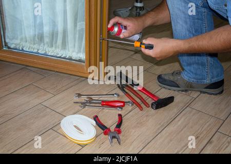 Immagine delle mani di un uomo di mano mentre ripara e spruzza lubrifica la serratura di una finestra della casa. Fai da te in casa. Foto Stock